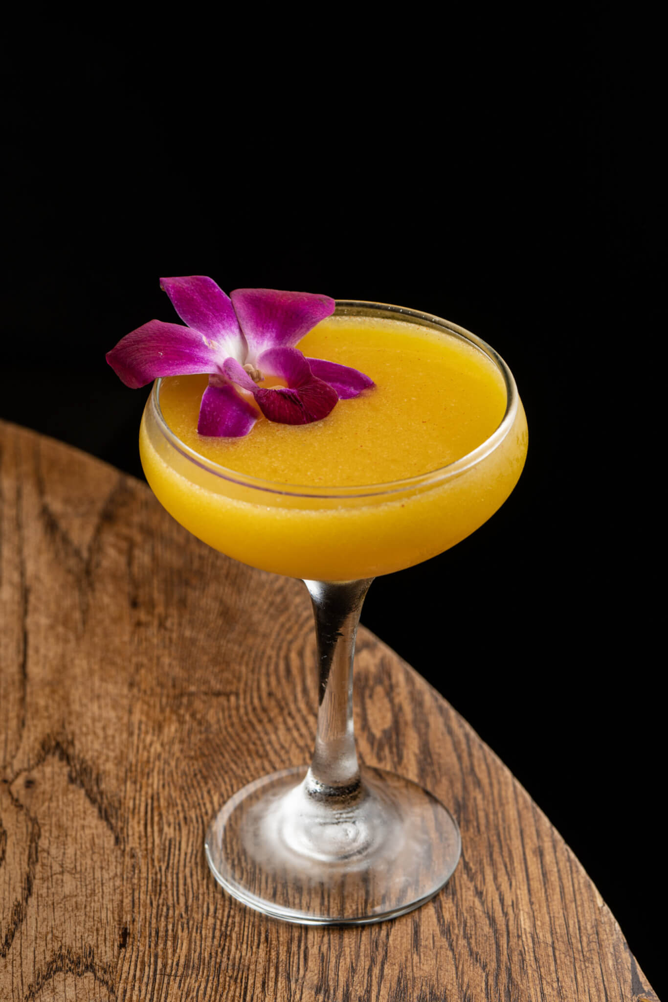 yellow cocktail with purple flower garnish