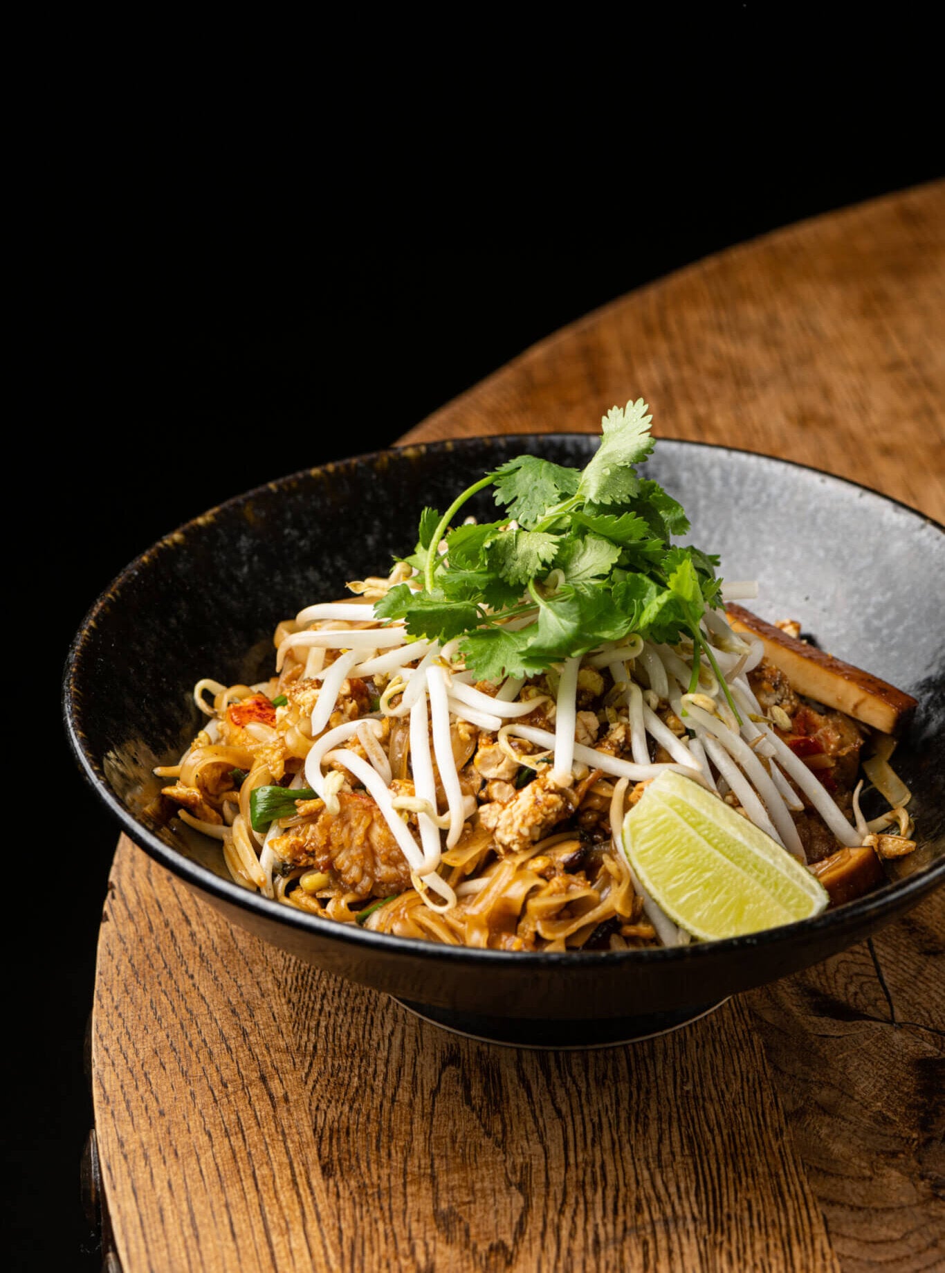 bowl of chicken pad thai topped with bean sprouts, cilantro and a lime wedge