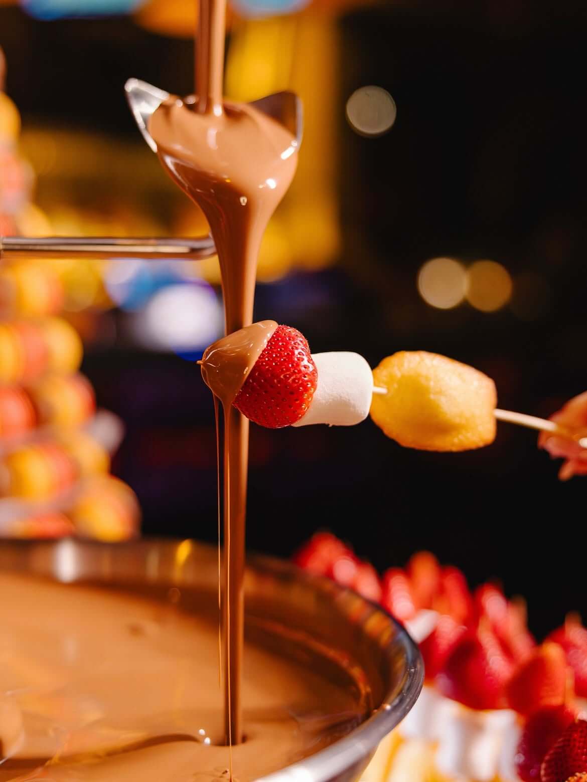 chocolate fountain with skewer of strawberry, marshmellos and madeline cookies