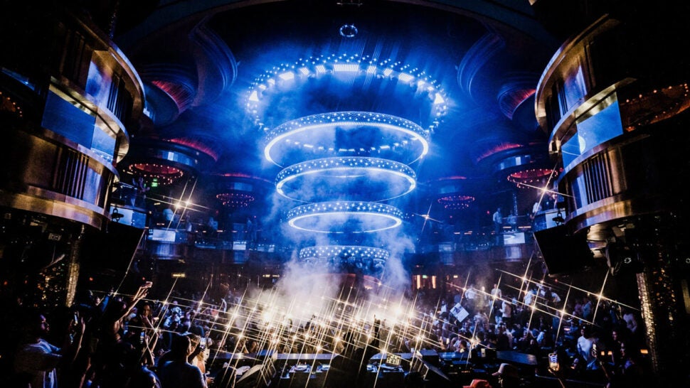 A crowded nightclub with blue circular lights above the dance floor, smoke effects, and sparkling lights among lively partygoers.